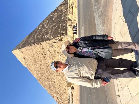       Couple stands arm-in-arm before the Great Pyramid of Giza under a brilliant blue sky.
  