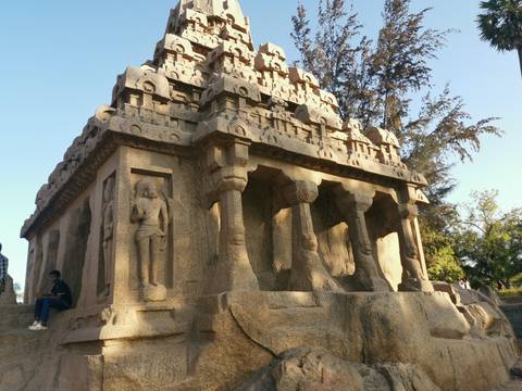       Granite monolithic temple of Pancha Rathas bathed in late afternoon light with visitors seated nearby.
  