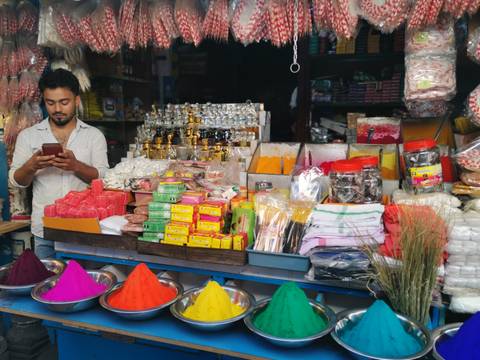       Young vendor checks his phone behind a colourful stall of spices, powders and trinkets.
  