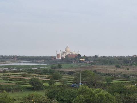       Distant view of the Taj Mahal across a river surrounded by flat countryside
  