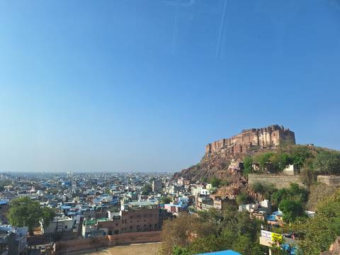       Mehrangarh-like fort dominates a rocky hill above sprawling blue-washed cityscape under clear sky
  
