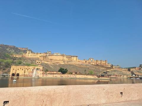       Amber Fort’s sandstone ramparts reflected in a calm lake beneath a vivid blue sky
  