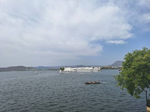       Lake Pichola with the white Lake Palace hotel afloat and boats cruising by
  