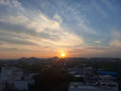       Sunset over city rooftops with distant hills silhouetted against glowing sky
  