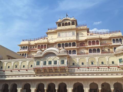       Facade of City Palace Jaipur with intricate balconies and cream-yellow walls under blue sky
  