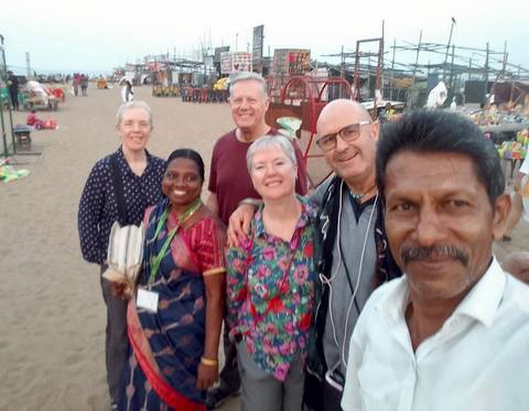       Slightly blurry selfie of tour group smiling on a busy beach with food stalls behind
  
