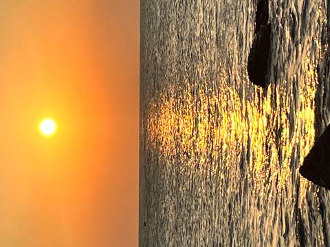       Brilliant orange sun sets over a calm sea casting a shimmering golden path on the water.
  