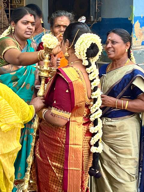       Bride in rich silk sari and jasmine garland participates in a lamp-lighting ceremony with family.
  
