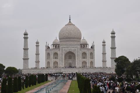       Front view of the Taj Mahal with large crowds gathered along the reflecting pool on an overcast day.
  