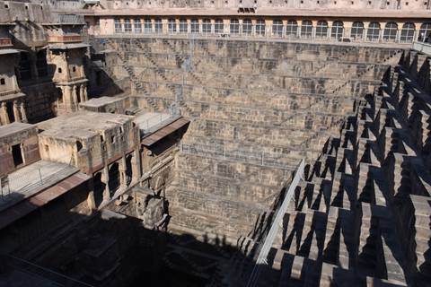       Deep geometric stone stepwell with intricate symmetrical stairs and pavilion niches.
  