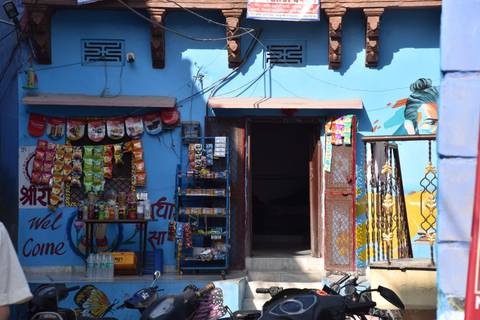       Small blue-painted neighbourhood shop displaying colourful snack packets and goods.
  