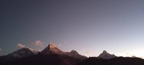       Dawn sky over silhouetted Himalayan peaks with subtle pink glow.
  