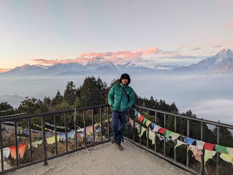       Traveller stands on a lookout deck festooned with prayer flags, above a hazy Himalayan vista.
  