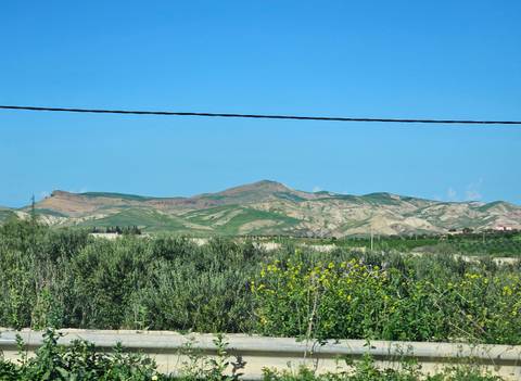       Distant rolling green hills under clear sky with power line crossing foreground.
  