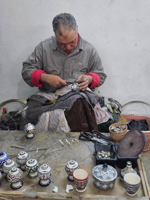       Artisan’s hands craft intricate metal filigree in workshop.
  