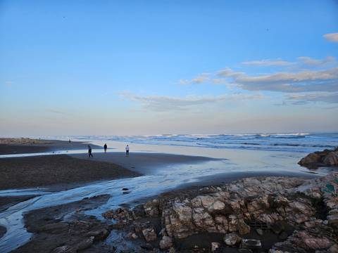       Locals stroll along wide sandy beach at dusk with gentle surf.
  