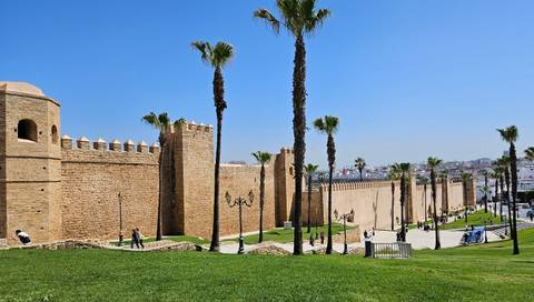       Long fortified wall with palm-lined promenade under bright blue sky in Rabat.
  
