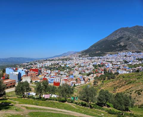       Panoramic view of Chefchaouen’s blue buildings spreading across foothills of Rif Mountains.
  