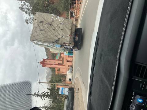       View through a car windshield of a winding mountain road with an overloaded truck and a red tower ahead under cloudy skies.
  