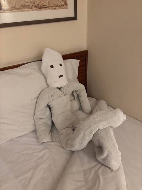       Playful towel sculpture shaped like a relaxed human figure on a hotel bed.
  