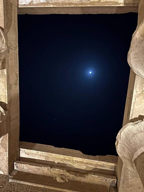       Night sky with bright moon framed by two massive stone columns in darkness.
  