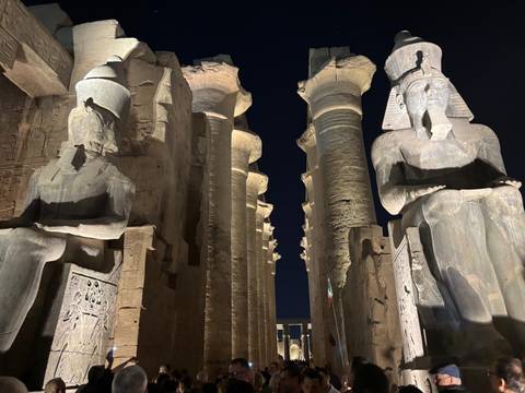       Nighttime view between colossal seated statues and towering columns at Luxor Temple.
  