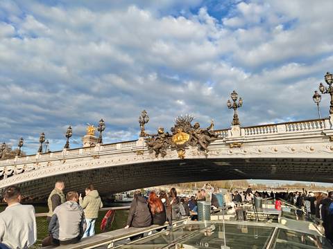       Elegant Pont Alexandre III bridge adorned with ornate sculptures and lampposts, crowded with tourists under a dramatic cloudy sky.
  