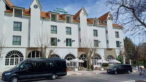       White three-storey hotel with arched windows and parked tour vans along a quiet town street.
  