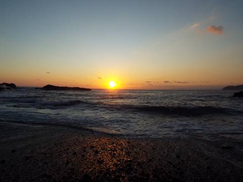       Serene ocean sunset with golden sun dipping below the horizon casting reflections on gentle waves.
  