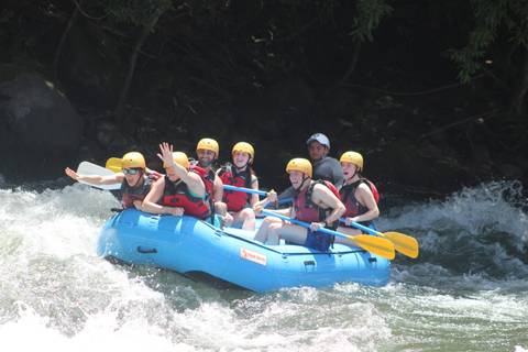       Thrilled rafters in a blue inflatable navigating white-water rapids surrounded by lush jungle.
  