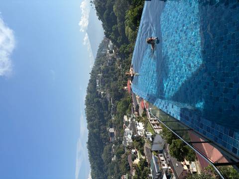       Travellers enjoy an infinity rooftop pool overlooking green hills and town
  