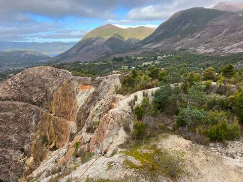       Rocky ravine and rugged hill slopes with township and distant lake framed by mountain backdrop
  