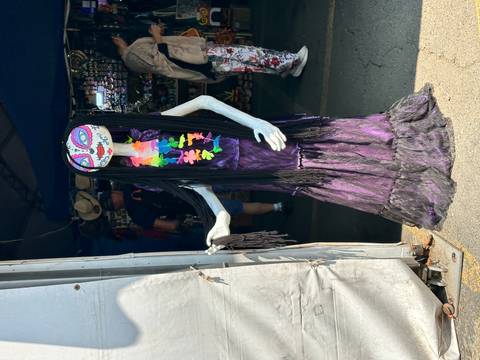       Tall Day-of-the-Dead style skeleton doll dressed in purple on display at an outdoor Mexican market stall
  
