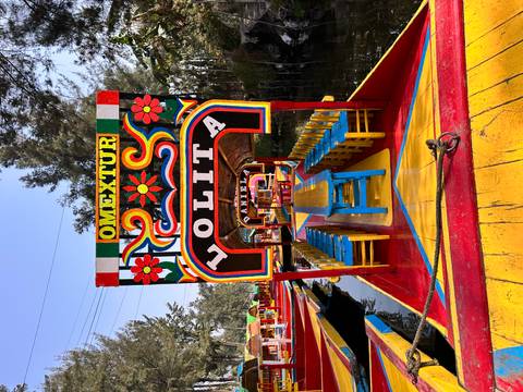       Brightly painted Xochimilco trajinera boat named “LOLITA” docked on a canal with vivid primary colors
  