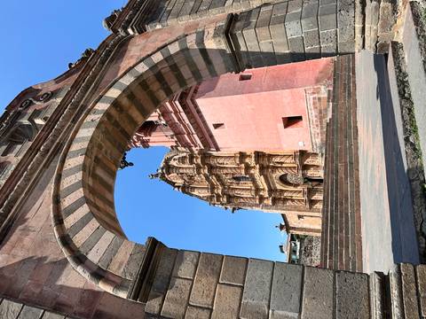       Stone archway perfectly framing a pink-hued colonial church façade under a bright blue sky
  