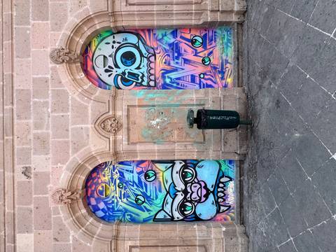       Colorful street art of cartoon monsters painted on two arched doorways in a stone wall
  