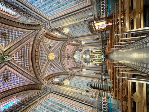       Grand ornately tiled church interior with soaring vaulted ceilings, chandeliers, and wooden pews leading to the altar
  