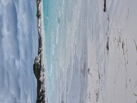      Pristine white-sand beach with turquoise waves and dunes beneath an overcast sky.
  