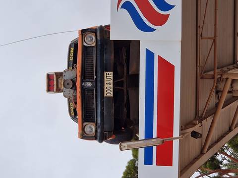       Old rust-colored ute mounted on a service-station roof with humorous licence plate.
  