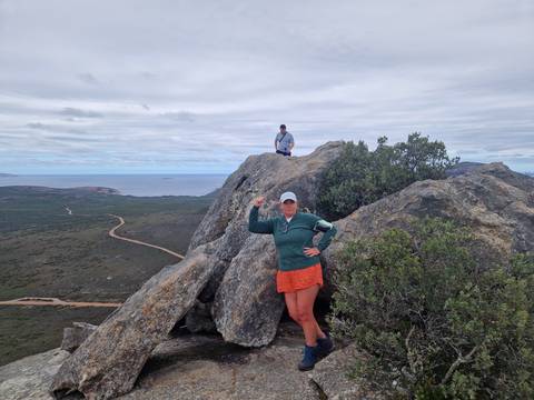       Hikers posing on a rocky summit overlooking coastal bushland and the ocean.
  
