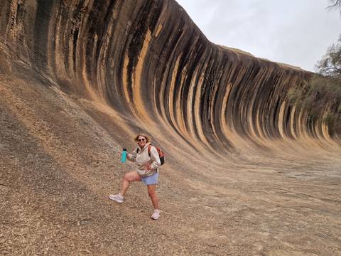       Tourist posing in front of the iconic striped rock formation of Wave Rock.
  