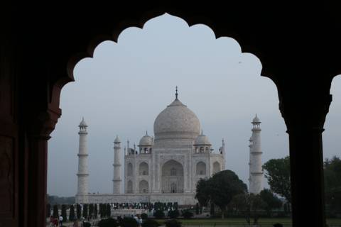       Iconic white marble Taj Mahal framed by a dark scalloped arch at dusk.
  