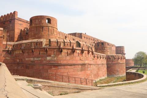       Massive red-sandstone ramparts and turrets of Agra Fort under hazy daylight.
  