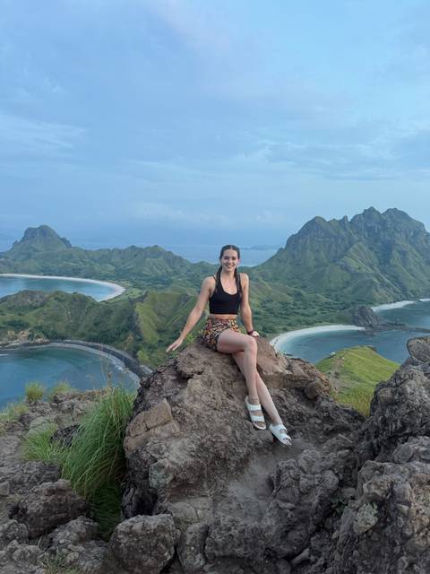       Woman sitting on a rocky summit overlooking the curved bays and green ridges of Padar Island.
  