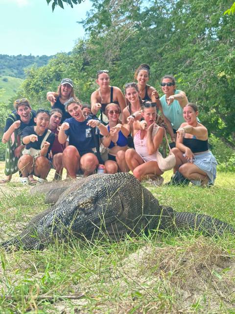       Excited group crouching behind a large Komodo dragon on grassy ground.
  