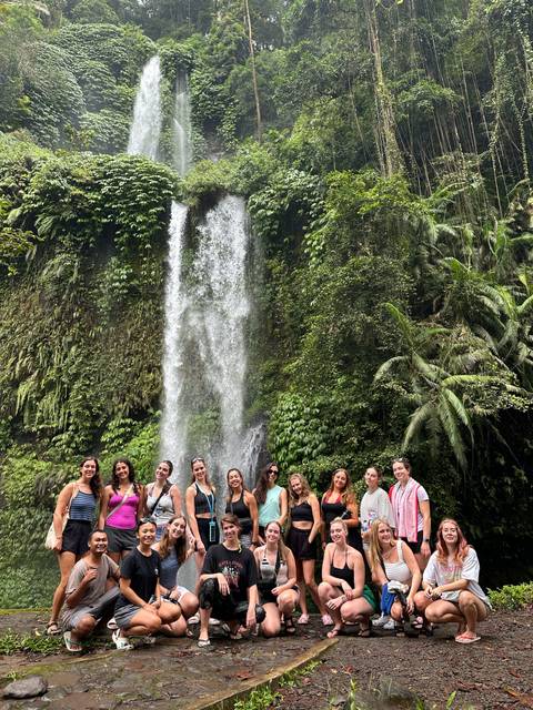       Travelers pose in front of a tall, lush jungle waterfall cascading down mossy cliffs.
  