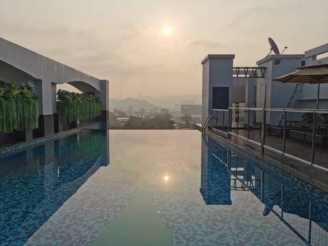      Rooftop infinity pool reflecting sunrise light with hazy cityscape and hills beyond.
  