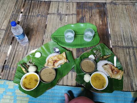       Traditional Assamese meal served on banana leaves with rice, curry, dal and accompaniments laid on a bamboo table.
  