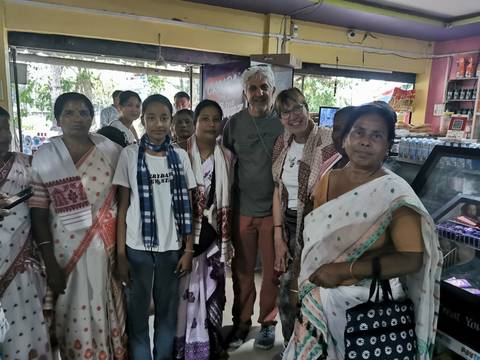       Tourists pose with local women in traditional Assamese dress inside a small roadside shop.
  
