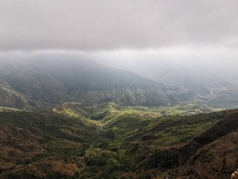       Misty mountain valley with dramatic layers of green ridges illuminated by shafts of sunlight through clouds.
  
